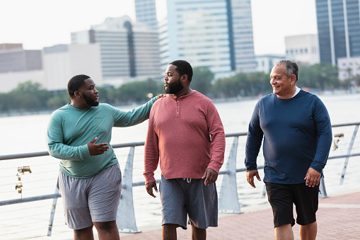 Three multiracial men walking, talking on city waterfront