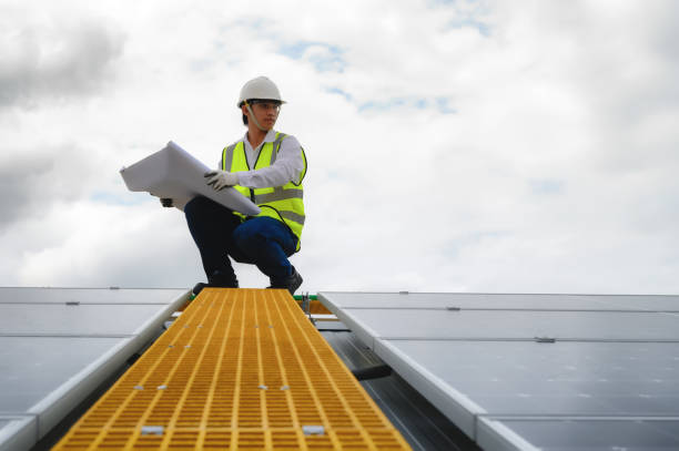 istock Young Engineers Open Drawing Blueprint Paper and Check Quality of Installing Solar Photovoltaic Panels on Rooftop of Building. 1574676538