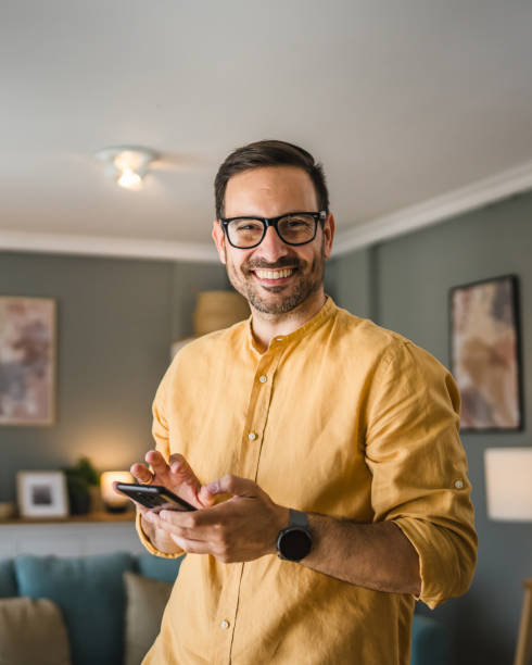One adult man with eyeglasses stand at home use mobile phone stock photo