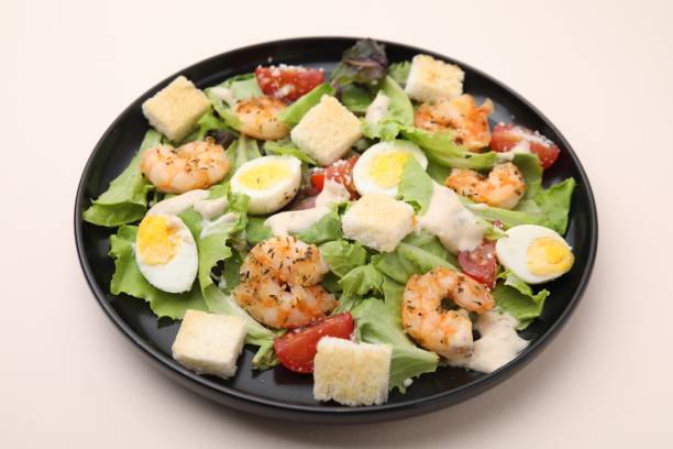 istock Delicious Caesar salad with shrimps on beige table, closeup 1574716166