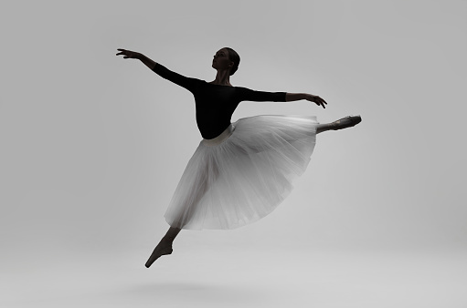 Beautiful ballerina dancing on light grey background. Dark silhouette of dancer