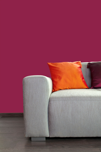 Contemporary gray material sofa with pillows against purple wall, wooden floor. Copy space, studio shot.
