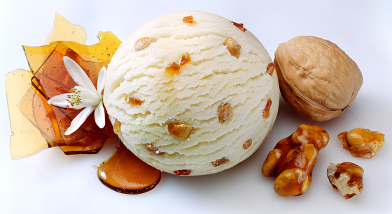 A Composition of a vanilla ice cream ball with pieces of caramelized  walnut inside and pieces of caramel and walnut around
