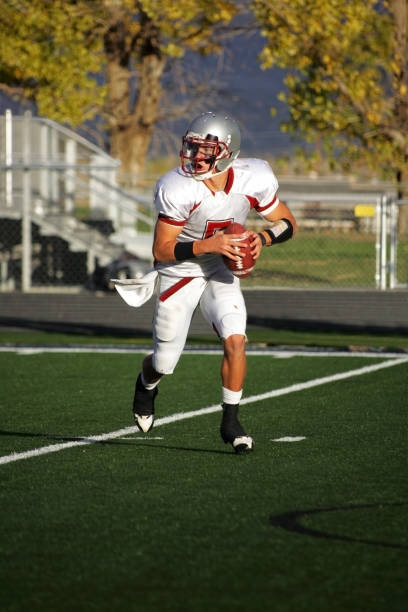 istock Young Male Quarterback Rolling Out Left with Football 157473614