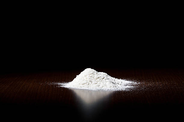A small pile of white powder on a dark surface White powderlokking like cocain on dark brown empty Kitchen table cocaine stock pictures, royalty-free photos & images