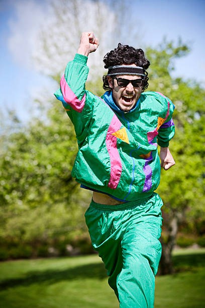 Mullet Runner With 1980's-1990's Fashion Style A man in a bright fluorescent sweat suit runs hard through a city park on a warm summer day decked out with a sweat band and tinted vintage glasses.  Nothing will get in the way of his vintage determination.  Vertical with copy space. sweat band stock pictures, royalty-free photos & images