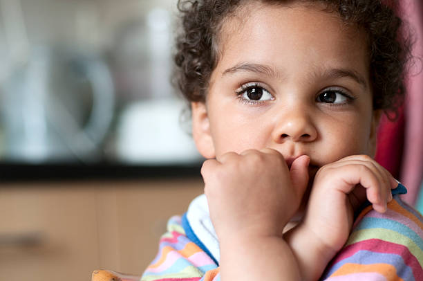Portrait of Very Thoughtful Little Girl Sitting in Kitchen Royalty free stock photo of 3 years old child. She has her arms crossed under her chin and over her mouth. Without looking at camera, she has a very thoughtful expression. critical thinking kids stock pictures, royalty-free photos & images