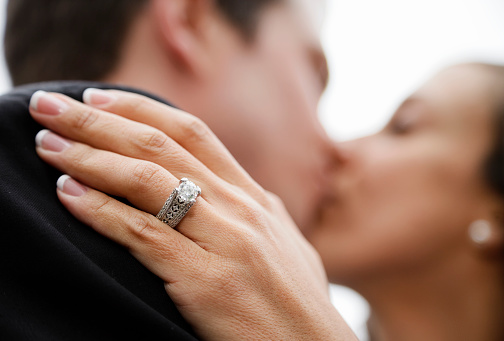 A bride and groom kissing with focus on the bride's wedding ring.