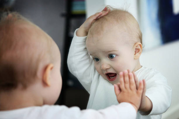 Baby looking at itself in a mirror  looking in mirror stock pictures, royalty-free photos & images