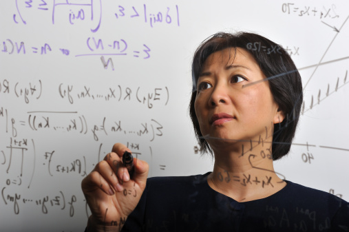 Portrait of Asian woman, in her 30s or 40s, working on some mathematical formulas on a translucent board.