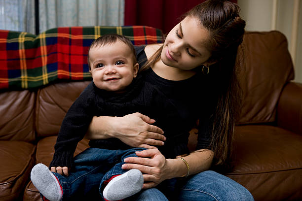 Adorable Baby Boy Sitting on Latina Mother's Lap at Home stock photo