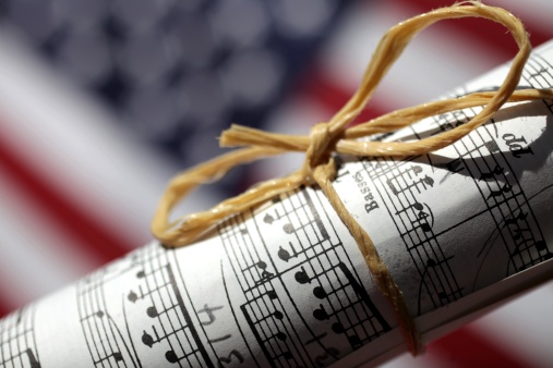 XXXL photo of a rolled up peice of sheet music with dramatic lighting in front of a blurred American Flag