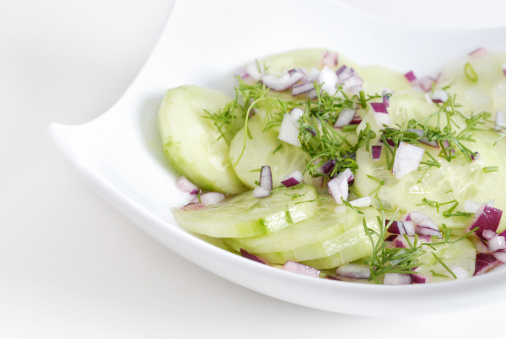 fresh salad made of cucumber, red onions, garnished with dill, in a white china bowl