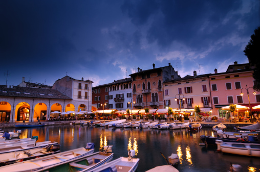 A summer evening with an upcoming thunderstorm in Desenzano del Garda, Lake Garda/Italy. People sitting at the harbor restaurants. 