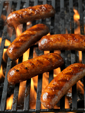 Sausages in a row on the grill are cooked on the grill of an open fire.