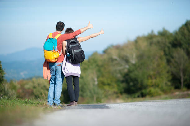 istock Young couple, backpackers, hitchhiking on a hilly road on a sunny day 1574774721