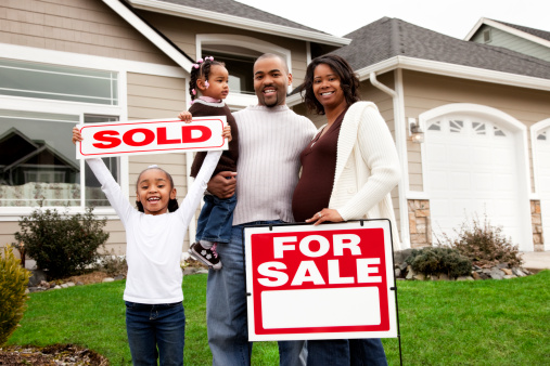 A latin descent Real Estate Agent sells or shows home to a young mixed race couple of African and Latin descents. They stand in front yard with real estate sign also in scene.
