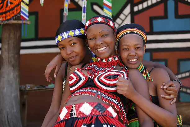 Three young Zulu women friends, dressed in traditional beaded Zulu garments, pose happily for the camera. The Zulu tribe is found mainly in Kwazulu-Natal, South Africa.