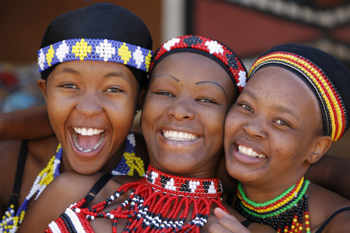 Three young Zulu women friends, dressed in traditional beaded Zulu garments, pose happily for the camera. The Zulu tribe is found mainly in Kwazulu-Natal, South Africa.