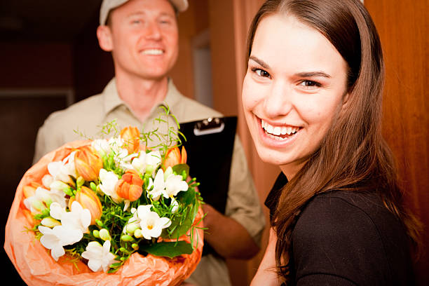a delivery boy is hading over a bouquet of flowers to a young female customer. focus is on the girl.