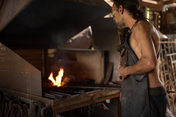 istock Blacksmith stoking the fire in the forge of his workshop. 1574787753