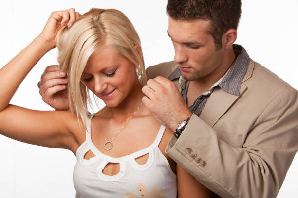 To give diamonds. Men's hands fasten a pendant with jewelry around the neck of their beloved. Beautiful young blonde in a black dress with a neckline.