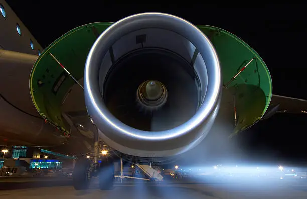 Airplane jet engine running with cowlings open during maintenance, exhaust gasses visible. Taken at night.