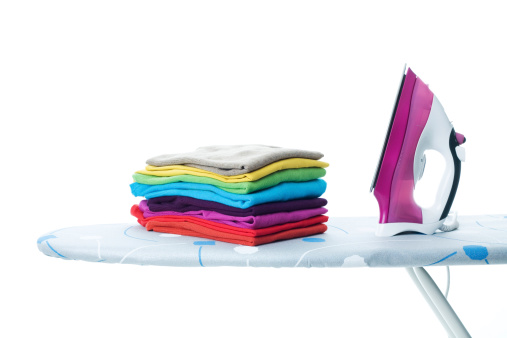 An iron sitting on a top of an ironing board next a pile of ironed clothes.