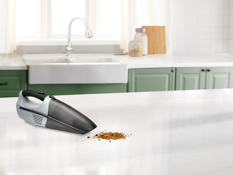 Small hand vacuum with dirt in a kitchen with a marble counter top and sink in the background