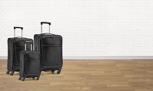 A set of black luggages in an empty room with hardwood flooring