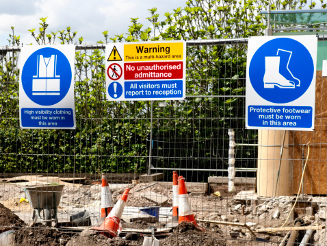 A variety of signs on a construction site fence.