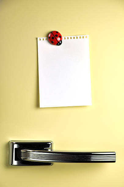 A yellow fridge with a white paper held by ladybug magnet stock photo
