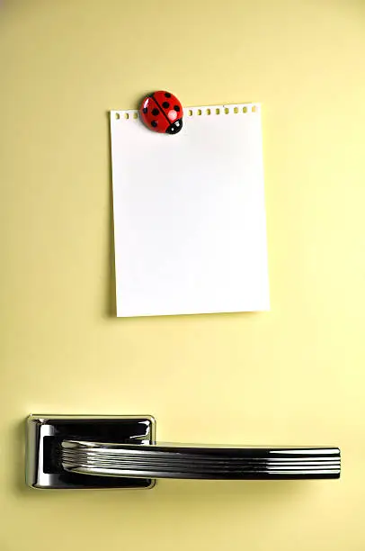 Photo of A yellow fridge with a white paper held by ladybug magnet