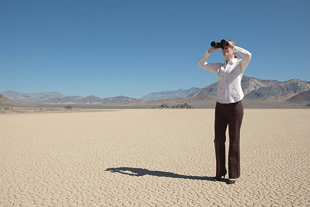 Woman looking through binoculars on a dry lake bed stock photo