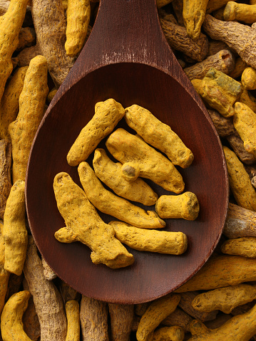 Top view of wooden spoon full of turmeric roots