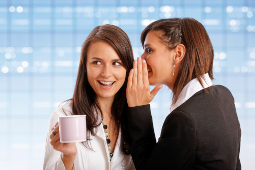 Coffee break: two young female office workers gossip in the office