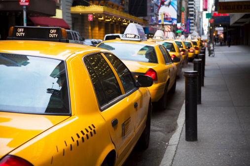 New York City, USA - July 31, 2018: Black driver waiting in a row of taxis on a street with people around and huge advertising screens in Manhattan, New York City, USA