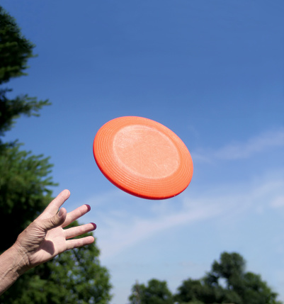 A single hand is reaching up to catch and orange frisbee against a blue sky.  Here are some other frisbee photos. 