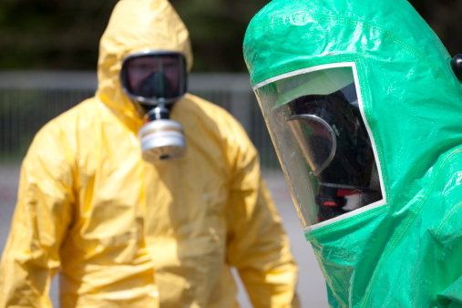Two men in protective gear cleaning up after chemical accident or radiation accident. The inflatable gear to the right protects against contamination with radioactive particles, against Alpha radiation and partially against Beta radiation. Focus on the right green person. Adobe RGB for better color reproduction.
