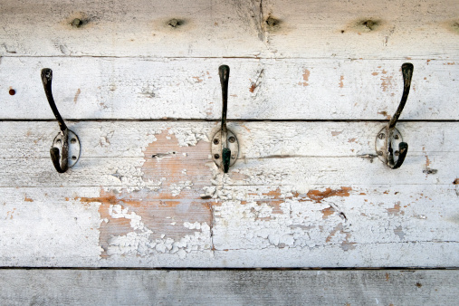 A row of old fashioned metal coat hooks on peeling painted wood.