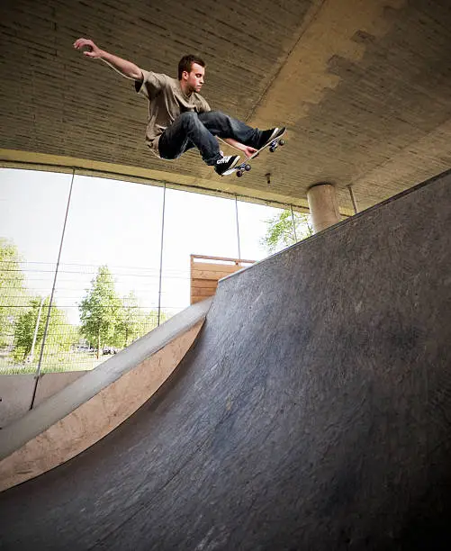 Wide angle photo of skateboarder doing a huge melon grab to fakey in the quarter pipe at a skate park. 