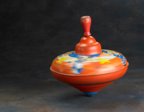 A antique child's toy top, spinning on a subdued painted background. Top is mostly blurred with motion.