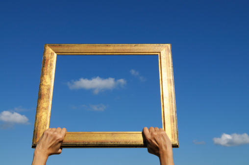 Woman holding an old frame against a blue cloudy sky. Blurred background