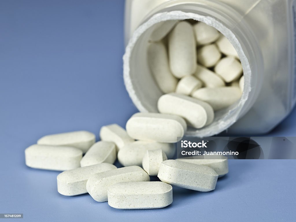 Tabletki wlewając, białe tabletki na niebieskim tle - Zbiór zdjęć royalty-free (Barwne tło)