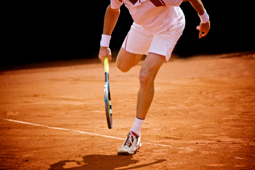 Detail of a tennis player running on a clay court.