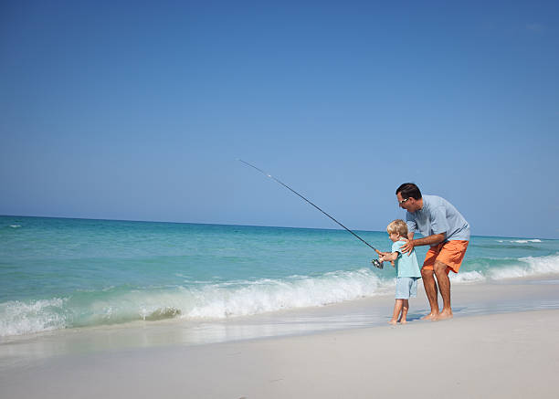 Father and small son fishing at the beach Father and his little boy fishing on the shore of a gorgeous beach. sea fishing stock pictures, royalty-free photos & images