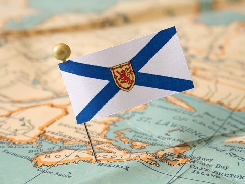 Paper flag of canadian Nova Scotia province pointing Halifax city over more that sixty years old map. Shallow depth of field