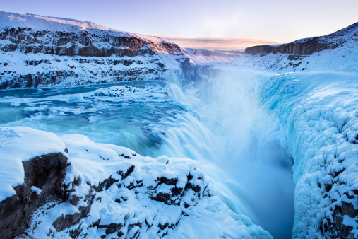 The Gullfoss Falls in Iceland photographed at a -20C / -4F temperature in mid winter. The falls are partially frozen and iced over. Photographed just after sunset when the sun colours the sky a beautiful purple, but doesn't reach the crevice anymore.