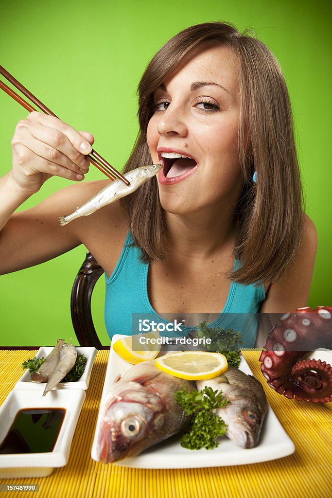 Sushi - Very Raw Young Caucasian woman in her twenties eats the rawest sushi imaginable, whole uncooked herring, perch, and octopus tentacles. Chopsticks Stock Photo