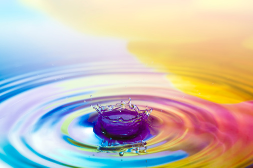A waterdrop falling down into the rippled colored water.